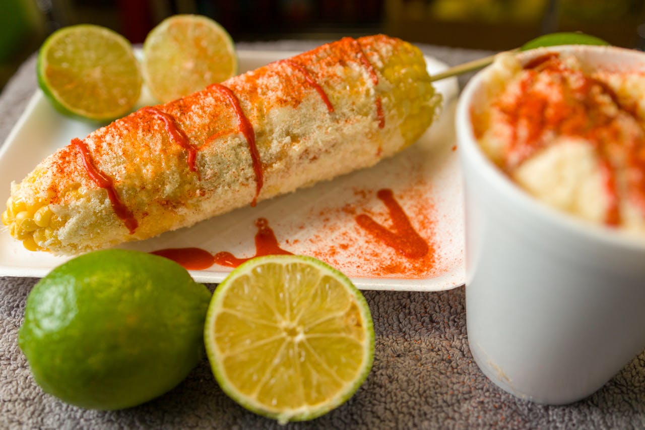 services-03 Close-up of Mexican elote topped with cheese and chili powder served with fresh lime.