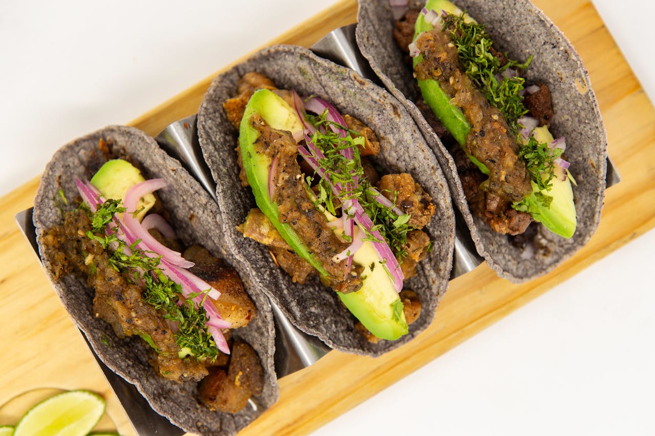 services-img Close-up of blue corn tacos with avocado and vegetables on a metal tray.