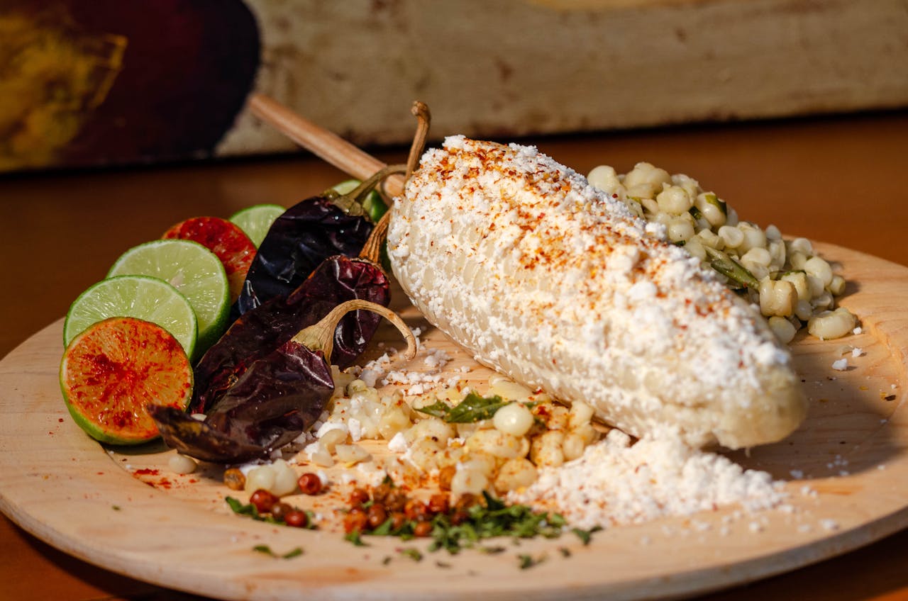 our-experience Delicious Mexican street corn, elote, served with chili, lime, and cheese toppings on a wooden plate.